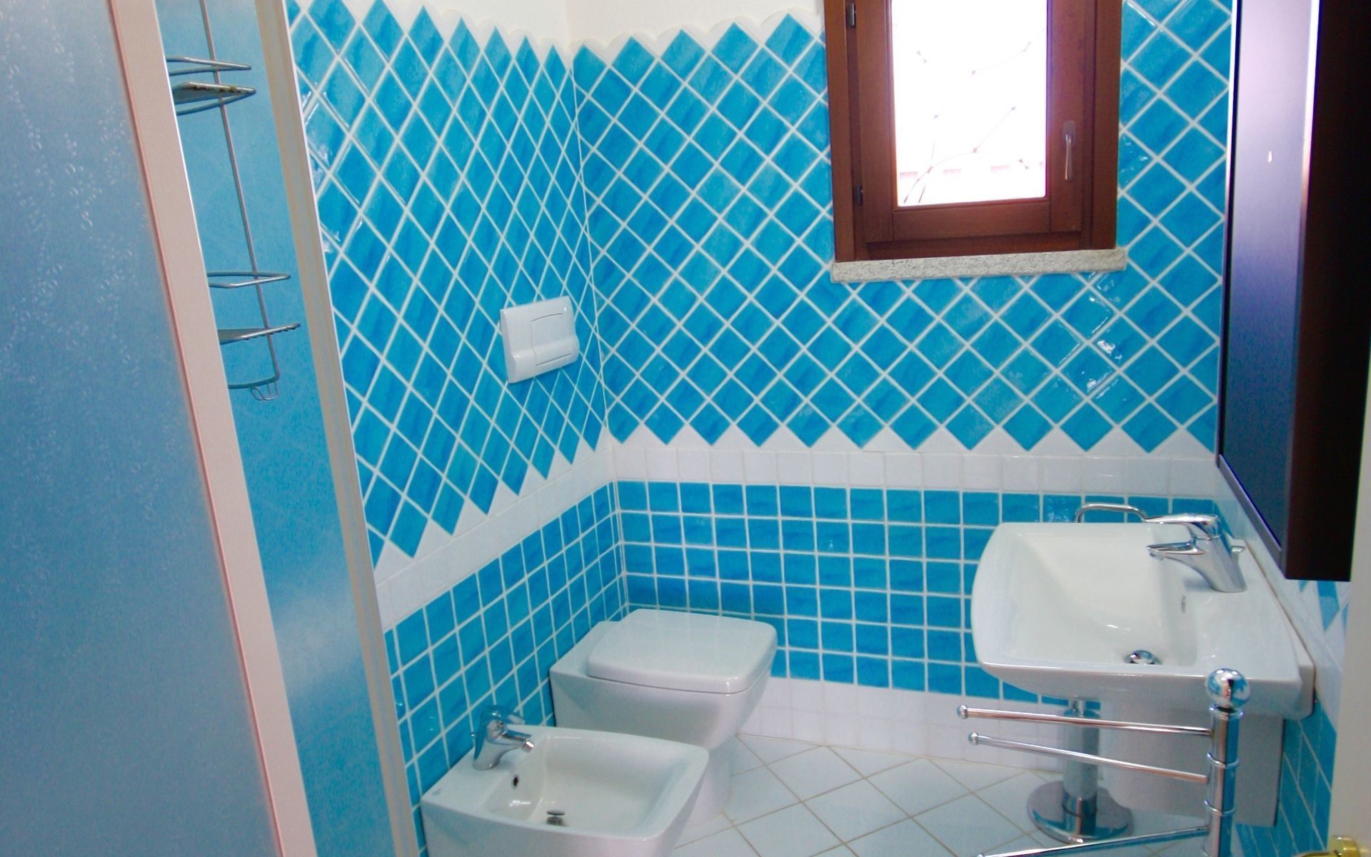 Une salle de bain avec des carreaux bleus à motifs losangés, des toilettes blanches, un lavabo blanc et une fenêtre.