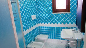 A bathroom with blue diamond-patterned tiles, a white toilet, a white sink, and a window. - Myrsine 2 (Olbia)