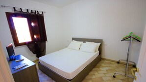 A small, clean room with a bed, a desk with a laptop, and a coat rack. - Myrsine 2 (Olbia)