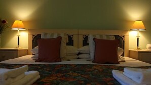 Une chambre d’hôtel avec un lit, deux tables de chevet, deux lampes et une couvre-lit à motifs floraux.