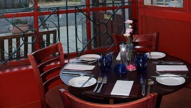 Un coin repas avec une table dressée pour quatre personnes, de grandes fenêtres offrant une vue dégagée et un mur extérieur de couleur rouge.