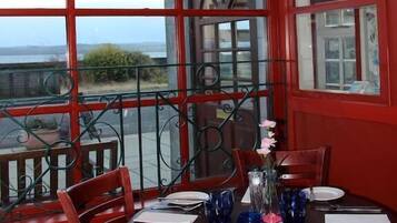 A dining area with a table set for four, large windows with a view, and a red exterior wall.