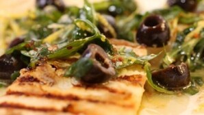 Une vue rapprochée d’un plat composé de viande grillée, de légumes verts et d’olives noires.
