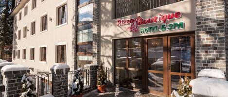 A building with a sign for "Rizzo Boutique Hotel & Spa" with a glass entrance and snow-covered surroundings.
