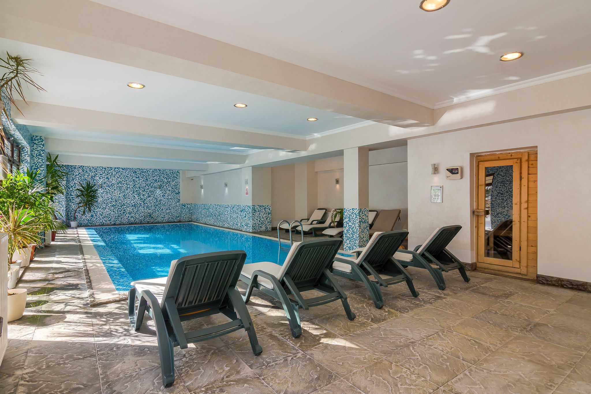 Una piscina interior con sillones de descanso, suelo y pared de azulejos.