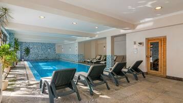 Una piscina interior con sillones de descanso, suelo y pared de azulejos.