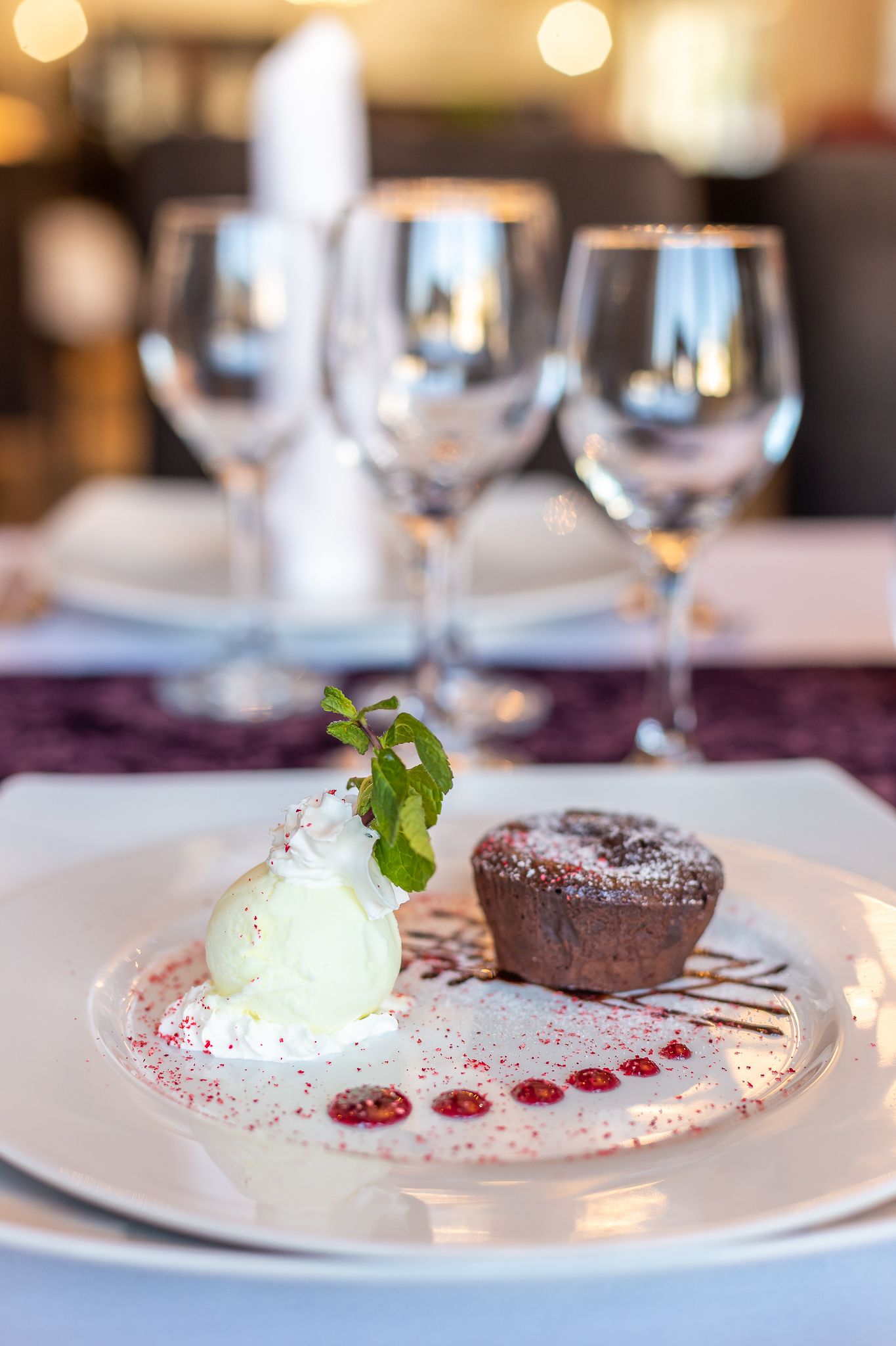 Un plato de postre con una bola de helado y un muffin de chocolate, adornado con hojas de menta y bayas rojas, sobre un plato blanco.