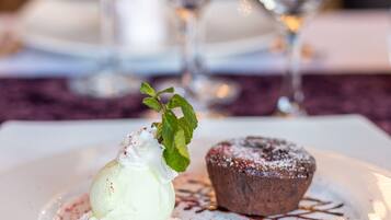 Un plato de postre con una bola de helado y un muffin de chocolate, adornado con hojas de menta y bayas rojas, sobre un plato blanco.