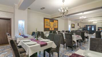A dining area with tables set for service, a chandelier, and a large painting on the wall.