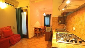 A compact kitchen with a gas stove, a dining table with chairs, and a red sofa. - Casa Assumptha Pt (Olbia)