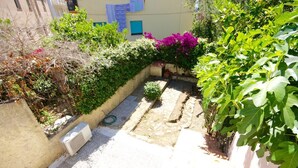A narrow courtyard with a stone pathway, surrounded by lush greenery and flowering plants. - Casa Assumptha Pt (Olbia)