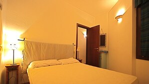 A bedroom with a bed, a nightstand, a lamp, a door, and a wall-mounted light fixture. - Casa Assumptha Pt (Olbia)