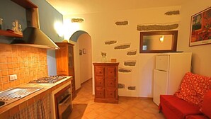 A compact kitchen with a gas stove, wooden cabinets, and a refrigerator. - Casa Assumptha Pt (Olbia)