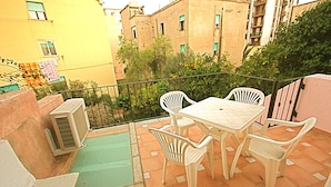 A balcony with a table and chairs, a small air conditioning unit, and a green mat. - Casa Assumptha 1p (Olbia)