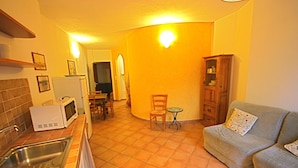 A compact kitchen with a dining area, a small table, and a sofa. - Casa Assumptha 1p (Olbia)