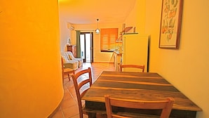 A dining area with a wooden table and chairs, a kitchen in the background, and a framed picture on the wall. - Casa Assumptha 1p (Olbia)