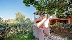 A stone staircase leading to a covered balcony with a railing, surrounded by greenery and a clear sky. - Casa Anna (San Teodoro)