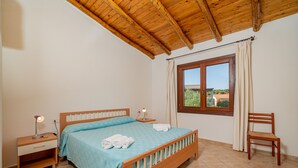 A bedroom with a wooden bed, nightstands, a chair, and a window with curtains. - Casa Anna (San Teodoro)