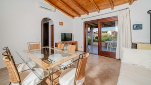 A modern living room with a glass dining table, wicker chairs, a white sofa, and a wooden ceiling. - Casa Anna (San Teodoro)
