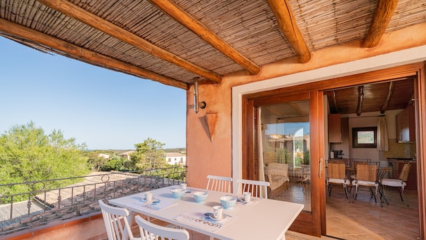 A balcony with a table set for dining, a wooden ceiling, and a view of the surrounding landscape. - Casa Anna (San Teodoro)