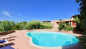 A swimming pool with a stone border, surrounded by a patio with lounge chairs. - Villa Ginepro (San Teodoro)