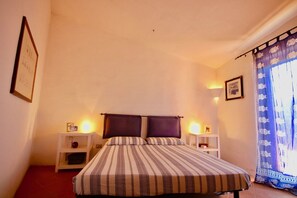 Quarto com uma cama, duas mesas de cabeceira, um criado-mudo, uma luminária na parede, um quadro emoldurado e uma cortina estampada.