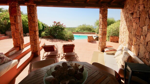 A covered outdoor seating area with stone pillars, a pool, and a view of the landscape. - Villa Ginepro (San Teodoro)