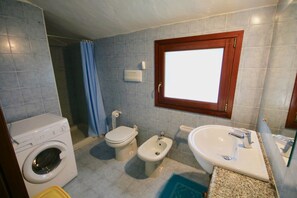 Un baño con lavadora, inodoro, bidé, lavamanos y una ventana con marco de madera.