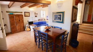 A dining area with a wooden table and blue chairs, a guitar, and a bowl of fruit on the table. - Villa Beatrice (Olbia)