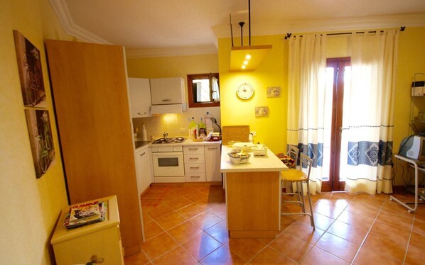 A compact kitchen with white cabinets, a central island, and a dining area with a chair.