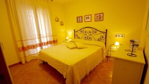 A room with a bed, two bedside tables with lamps, a wall with framed pictures, and a curtain. - Casa Antonella (Olbia)