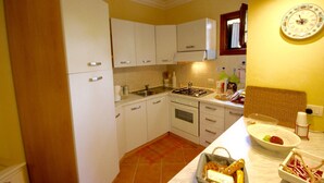 A compact kitchen with white cabinets, a gas stove, and a sink. - Casa Antonella (Olbia)