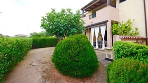 A building with a covered outdoor seating area, a paved pathway, and neatly trimmed hedges. - Casa Antonella (Olbia)