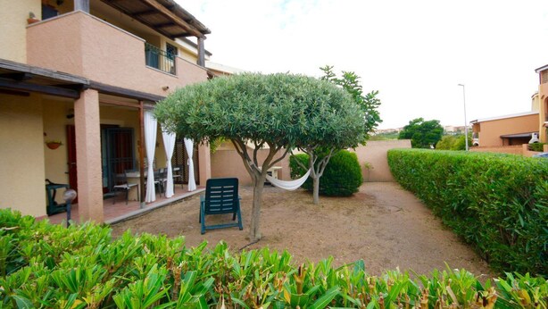 A building with a covered patio, a tree, and a chair. - Casa Antonella (Olbia)