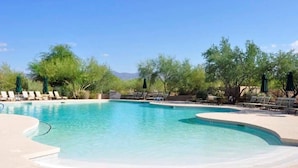 Une piscine entourée de chaises longues et de parasols, avec des arbres tout autour et des montagnes en arrière-plan.