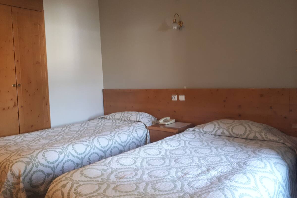 A room with two beds, a wooden wardrobe, a wall-mounted light fixture, and a telephone.