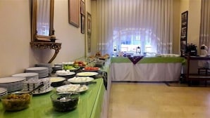 Una mesa de buffet con diferentes alimentos y platos, un mantel verde y una ventana con cortinas al fondo.