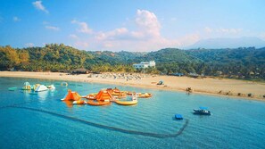 A beach with clear blue water, orange floating structures, and a sandy shore with umbrellas and beach chairs. - Camaya Coast Hotel (Mariveles)