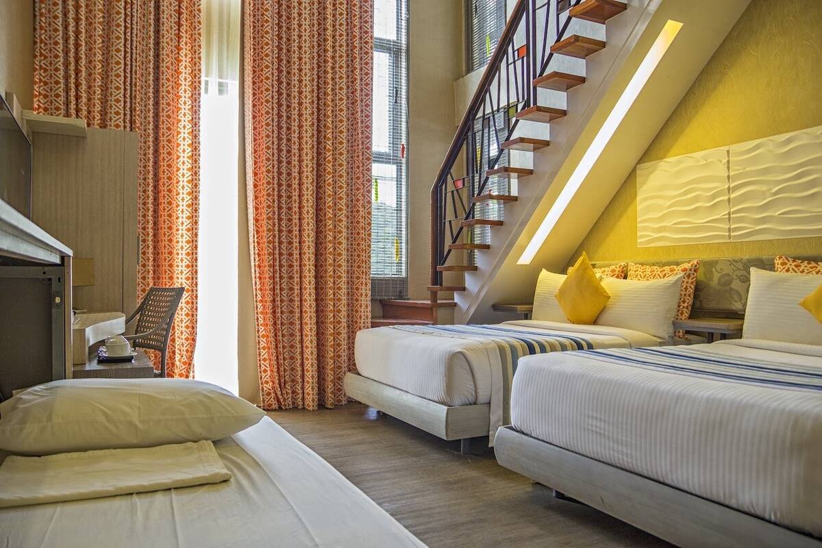 A hotel room with two beds, a desk, a chair, and a staircase.