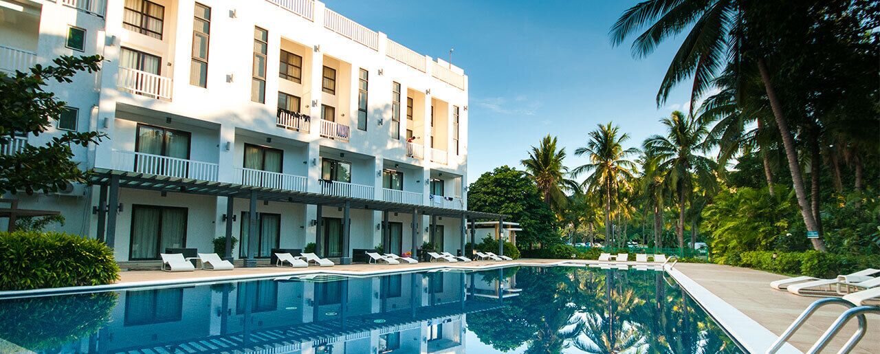 A hotel with a pool, multiple balconies, and palm trees.