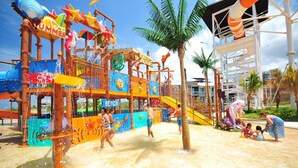 A vibrant water park with a slide, a beach area, and a palm tree. - Camaya Coast Hotel (Mariveles)