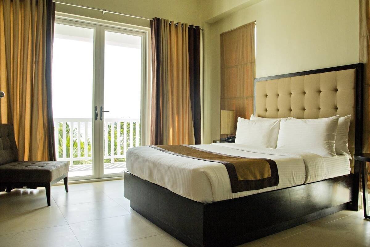A hotel room with a large bed, a chair, a nightstand, and a view of the outdoors.
