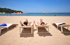 Trois transats sur une plage de sable, avec un ciel bleu dégagé et une mer calme en arrière-plan.