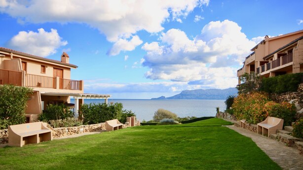 A well-maintained lawn with outdoor seating, a view of the sea, and buildings with balconies. - Casa Athena (Olbia)