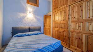 A bedroom with a bed, wooden wardrobe, and a wall-mounted light fixture. - Casa Athena (Olbia)