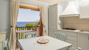 A kitchen with a view of the sea, a dining table, and light-colored cabinets. - Casa Athena (Olbia)