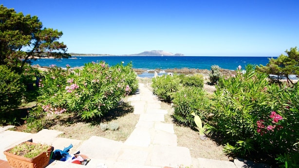 A stone pathway leading to a scenic view of the sea with a mountain in the distance. - Villa Magica (Olbia)
