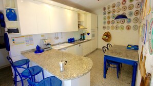 A compact kitchen with white cabinets, a granite countertop, a coffee machine, and a wall adorned with decorative plates. - Villa Magica (Olbia)