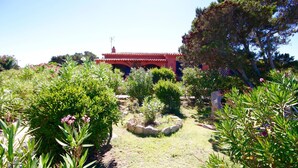 A traditional building with a red roof, surrounded by a well-maintained garden with various shrubs and a central stone feature. - Villa Magica (Olbia)
