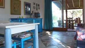 Una habitación con un escritorio azul, una computadora y una silla. Se ve una ventana con vistas al exterior.